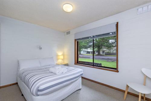 a white bedroom with a bed and a window at Eastern Beach Unit 1 in Port Fairy