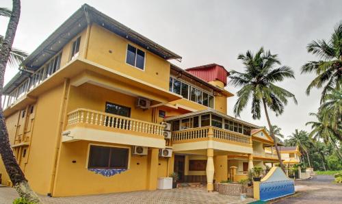 um edifício amarelo com palmeiras em frente em Treebo Trend Majestic Palms 2 Km From Colva Beach em Benaulim