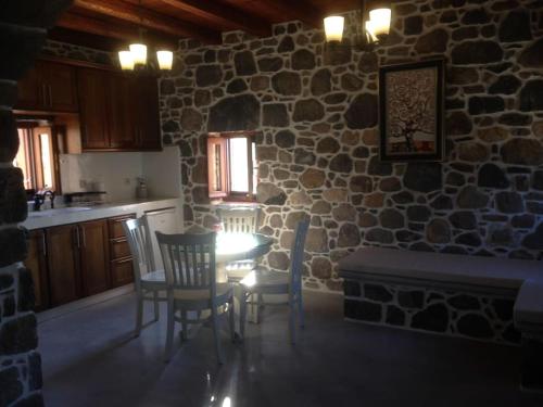 a kitchen with a table and chairs and a stone wall at Loutra Olive Garden Stone House #3 in Mandrakion