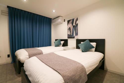 2 łóżka w pokoju hotelowym z niebieskimi zasłonami w obiekcie TAKETO STAY Sumikawa House w mieście Sapporo