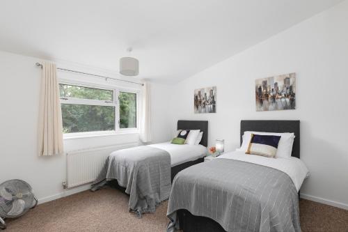 Duas camas num quarto com paredes brancas e uma janela em Skyvillion - STEVENAGE SPACIOUS COMFY 2BED HOUSE with Garden, Free WiFi & Parking em Shephall