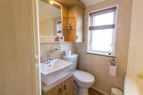 a bathroom with a toilet and a sink and a window at Beautiful, Pet Friendly Caravan By The Beach In Suffolk Ref 40126nd in Lowestoft