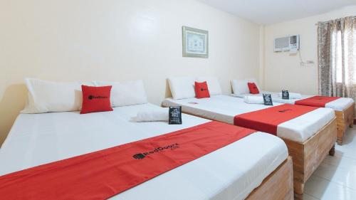 três camas num quarto com lençóis vermelhos e brancos em RedDoorz @ Goldland Spring Resort Urdaneta City em Urdaneta