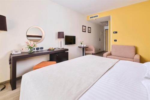 a hotel room with a bed and a desk and a mirror at Hotel Garden Istra Plava Laguna in Umag