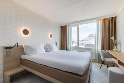 a hotel room with a bed and a desk and a window at Hotel de Baak Seaside in Noordwijk aan Zee