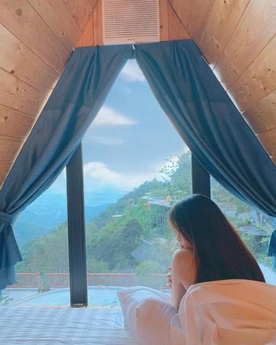 a woman laying on a bed looking out a window at Ban Mai Xanh homestay Tam Đảo in Vĩnh Phúc