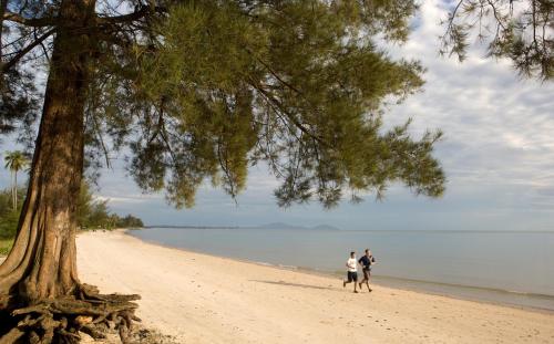 two people walking on a beach next to a tree at Novotel Bangka Hotel & Convention Center in Pangkalpinang