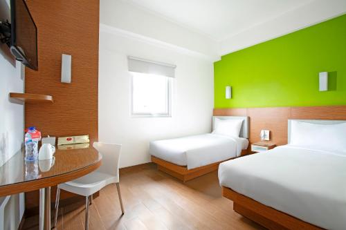 a hotel room with two beds and a desk with a table at Amaris Hotel Teuku Umar in Denpasar