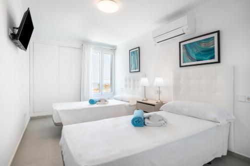a white bedroom with two beds and a window at Villa Enderrossall in Porto Cristo