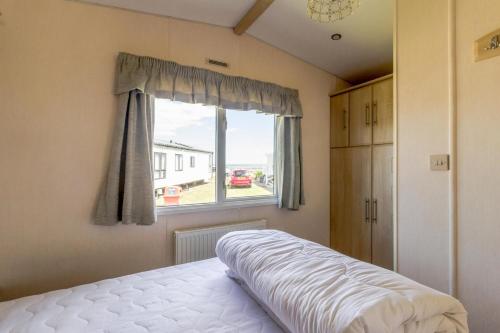 a bedroom with a bed and a window at By The Seaside Dog Friendly Caravan At Haven Hopton In Norfolk Ref 80015w in Great Yarmouth