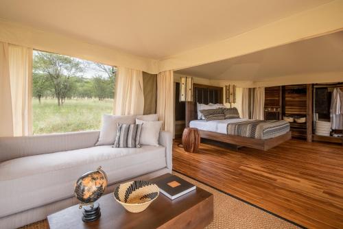 ein Wohnzimmer mit einem Sofa und einem Bett in der Unterkunft Cherero Camp in Serengeti-Savanne