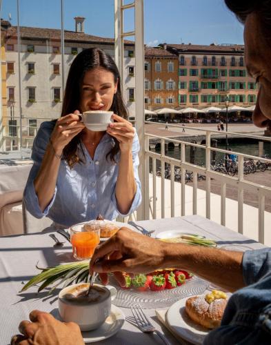 una mujer sentada en una mesa bebiendo una taza de café en Hotel Europa - Skypool & Panorama, en Riva del Garda