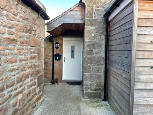 an alley with a white door and a brick wall at Glen Cottage 8 Fenton Hill Farm in Wooler