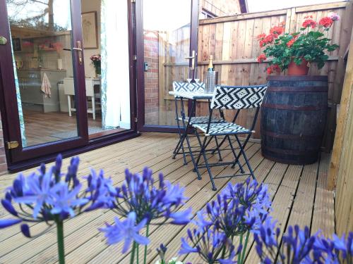 eine Veranda mit blauen Blumen und Stühlen sowie einem Fass in der Unterkunft Avocet Lodge, Snettisham in Kings Lynn