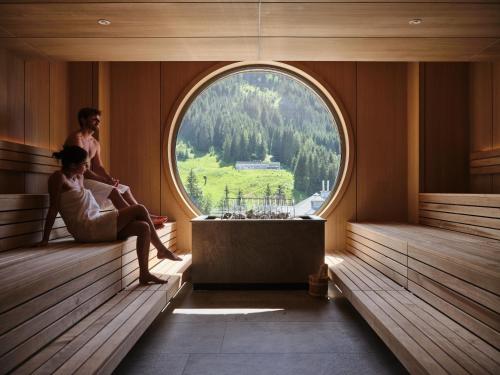 two people sitting on benches in a room with a window at Sporthotel Wagrain in Wagrain