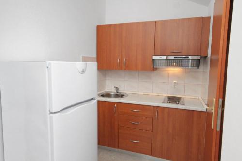 a kitchen with wooden cabinets and a white refrigerator at Apartment Njivice 5458b in Njivice