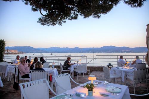 a group of people sitting at tables in a restaurant overlooking the water at Hôtel Les Mouettes - Teritoria in Ajaccio
