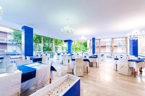 un restaurante con mesas y sillas blancas y ventanas en Mantovani Hotel Murano & Mariù en Rímini