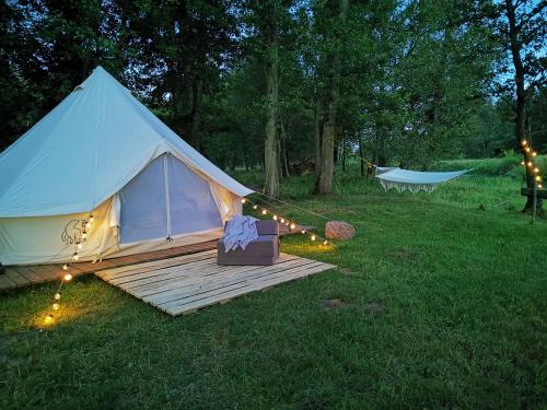 a white tent with a wooden deck in the grass at Glamping Kaliska in Łochów