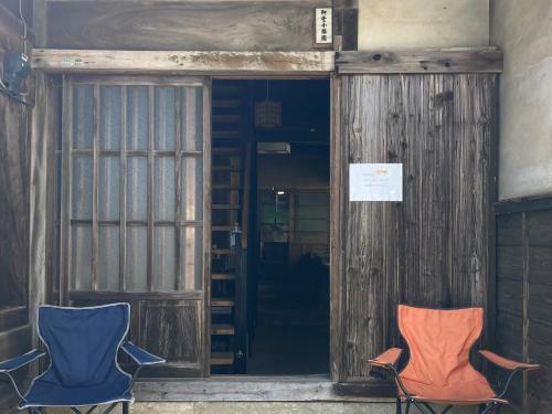 two chairs sitting in front of a door at ゲストハウス大安吉田 in Matsuzaki