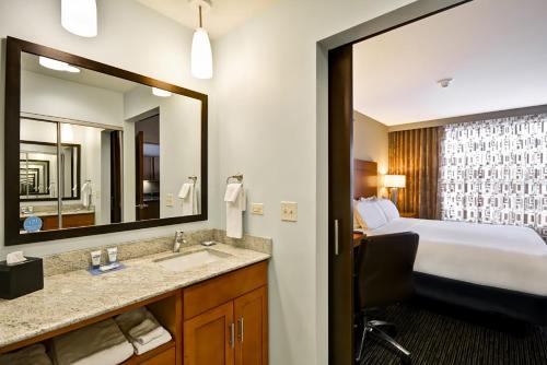 a hotel room with a bed and a sink and a mirror at Hyatt House Naperville/Warrenville in Warrenville