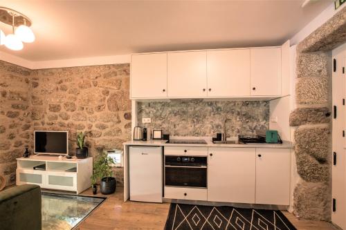 a kitchen with white cabinets and a tv on a wall at Mill House by the River in Arcos de Valdevez