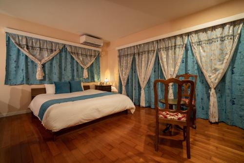 ein Schlafzimmer mit einem Bett mit blauen Vorhängen und einem Stuhl in der Unterkunft Palm Villa Ishigakijima karei in Ishigaki-jima