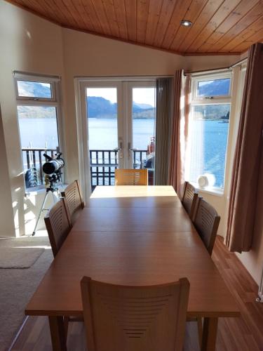 a dining room table with chairs and a view of the ocean at Bonnie Banks Lodge Ardlui in Ardlui