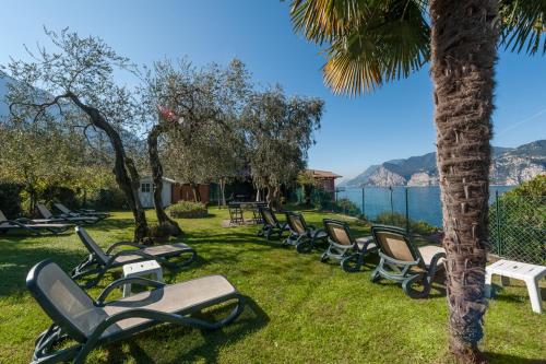 a row of chaise lounges on the grass near the water at Hotel Villa Carmen in Malcesine