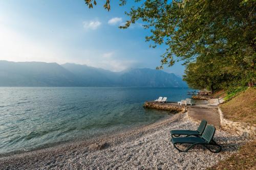 a green chair sitting on a beach next to the water at Hotel Villa Carmen in Malcesine