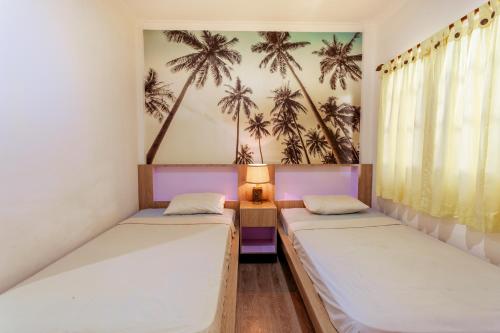 2 camas en una habitación con palmeras en la pared en Segara Sadhu Inn Kuta by ecommerceloka, en Kuta