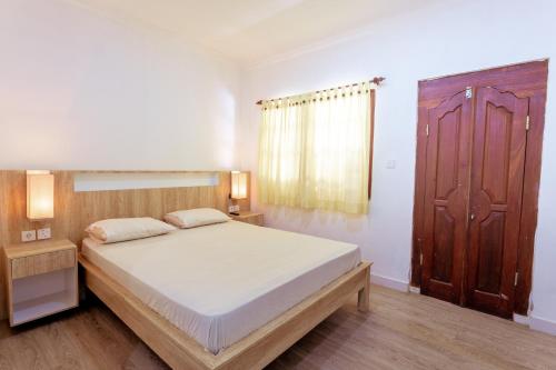 a bedroom with a large bed and a wooden door at Segara Sadhu Inn Kuta by ecommerceloka in Kuta