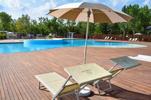 duas cadeiras e um guarda-sol em frente a uma piscina em Rimini Family Village em Rimini