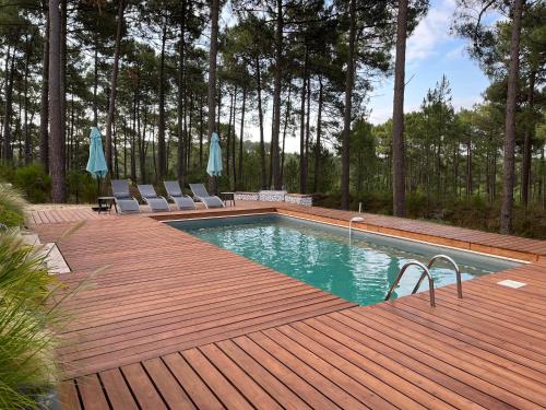 ein Pool auf einer Holzterrasse mit Stühlen in der Unterkunft Villa du Golf Eden Parc in Lacanau-Océan