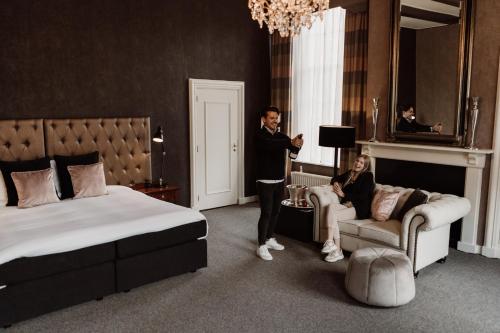 a man standing in a hotel room with a woman sitting on a couch at Châteauhotel De Havixhorst in Schiphorst