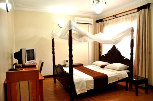 a bedroom with a canopy bed and a television at Olive Gardens Hotel Kampala in Kampala