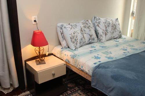 1 dormitorio con cama y mesita de noche con lámpara en Casa Mendes en Gramado