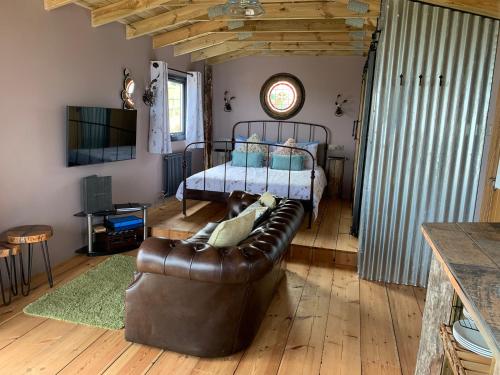 a living room with a leather couch and a bed at Byre Cottages & Log Cabin in Cardigan