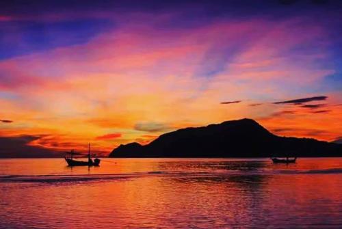 two boats in the water with a sunset in the background at Baan Golden Pool Villa in Sam Roi Yot