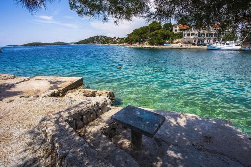 a bench sitting on the edge of a body of water at Seaside family friendly house with a swimming pool Razanj, Rogoznica - 19735 in Rogoznica