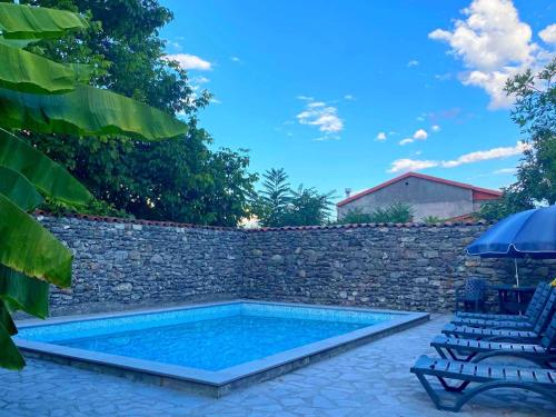 una piscina accanto a un muro di pietra con due sedie e un ombrellone di Hotel Villa Eniseli a Eniseli