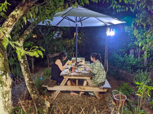 zwei Frauen sitzen an einem Picknicktisch unter einem Schirm in der Unterkunft Plum Hill - Moc Chau in Mộc Châu
