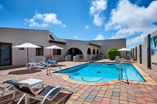 uma piscina com cadeiras e guarda-sóis ao lado de uma casa em Bubali Luxury Apartments - Adults Only - Wheelchair Friendly em Palm-Eagle Beach