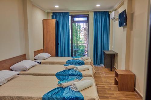 a row of four beds in a room with blue curtains at Villa Story Hotel in Shekvetili