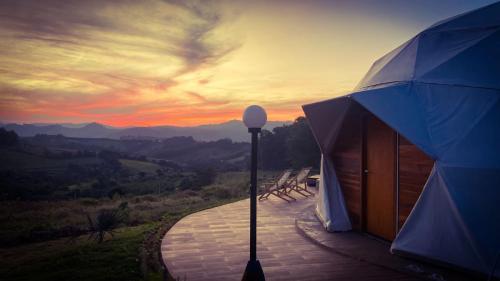 - une vue sur le coucher du soleil depuis un bâtiment avec un parasol dans l'établissement Domo geodésico_conforto e relaxamento na natureza, à Socorro