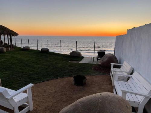 two white benches sitting next to the ocean at sunset at Triton's Playhouse Beachfront in Primo Tapia