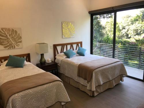 2 camas en una habitación con ventana grande en Casa Huitzil - La mejor casa de Malinalco con alberca y jacuzzi climatizados, en Malinalco