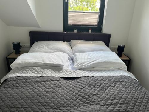 a bed with four pillows on it with a window at Apartamenty Pod Sosnami in Sarbinowo