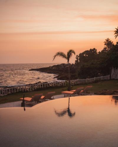a pool with chairs and a palm tree next to the ocean at Belika Beach in Hiriketiya