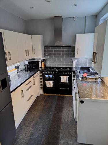 a kitchen with white cabinets and black appliances at Entire town house with free parking in Oswestry